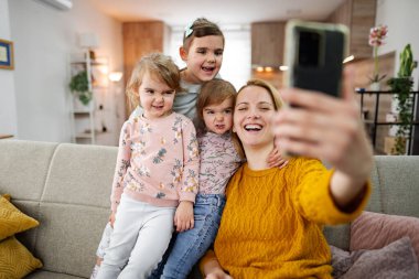 Anne ve üç kızı kanepede oturup evdeki oturma odasında selfie çekiyorlar..