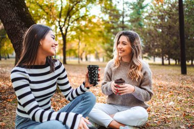 Kızlar, güzel bir sonbahar parkında yere düşmüş yaprakların arasında keyif çatan ve neşe saçan sıcak içeceklerden hoşlanırlar..