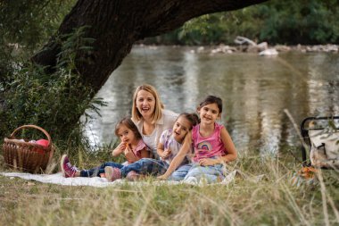 Üç kızı olan mutlu bir aile bir ağacın gölgesinde piknik yapıyor.