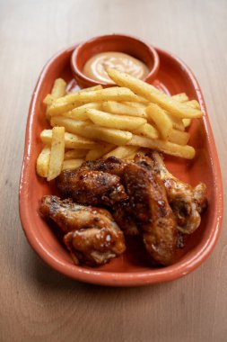 Lezzetli bir şekilde jölelenmiş tavuk kanatları, gevrek patates kızartması ve zengin bir sos ile kaplanarak ağız sulandırıcı bir yemek lezzeti yaratıyor..