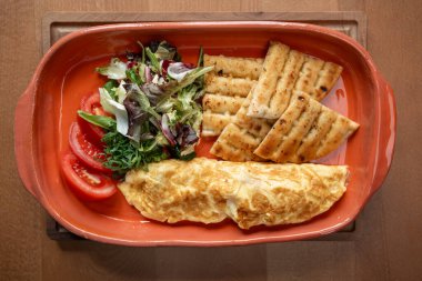 Canlı bir tabakta, gevrek salata, sulu domatesler ve kızarmış ekmeğin yanında pofuduk bir omlet sunuluyor. Lezzetli bir yemek deneyimi yaratıyor..