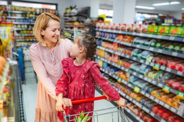 Mutlu anne-kız bir alışveriş arabasını market koridorunda iterken kaynaşıyor.