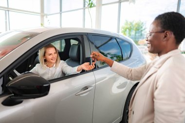 Otomobil galerisindeki bayandan araba anahtarı alan mutlu bir kadın.