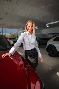 Yeni otomobil seçen mutlu kadın, galeride kırmızı araca bakıyor.