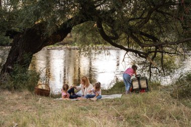 Anne ve kızları nehir kenarında söğüt ağacının altında piknik yapıyorlar.