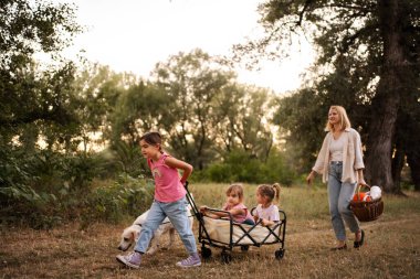 Anne ve kızları köpekleri ve arabalarıyla ormanda yürüyorlar.