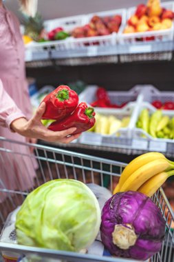 Woman choosing fresh produce in a supermarket, filling her shopping cart with vegetables