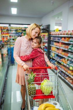 Mother and daughter sharing a loving hug while pushing a shopping cart full of groceries