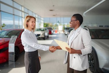 Two women shaking hands in a car showroom after a successful negotiation