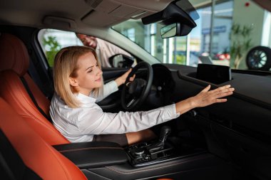 Woman sitting in a new car, touching the dashboard, while a salesperson looks on