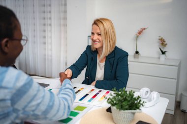 Two women exchanging handshake at desk, collaborating on a design project