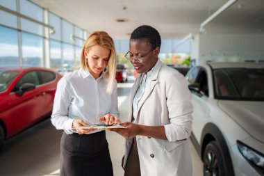 İki kadın bir araba galerisinde evrakları gözden geçiriyorlar.