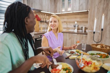 İki arkadaş sıcak bir mutfakta kahkaha ve lezzetli yemekleri paylaşıyor..