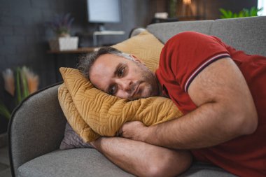 Evde yalnız bir adam kanepeye uzanmış üzgün ve perişan görünüyor..