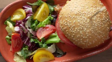 Hamburgerin yakın çekimi ve terasotta tabağında taze karışık yeşil salata.