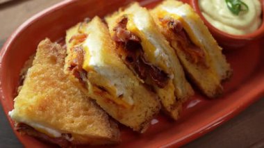 Çedar peynirli, pastırmalı ve kremalı soslu kızarmış yumurtalı ekmek sandviçi.