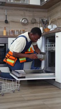 Ev mutfağındaki bozuk bulaşık makinesinin filtresini değiştiren üniformalı, çalışkan bir tamirci.