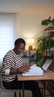 Genç Afrikalı iş kadını dizüstü bilgisayarda çalışıyor ve ev ofisteki not defterine not alıyor.