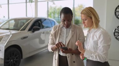 Araba satıcısı ve bir müşteri bir araba galerisindeki akıllı telefondan bilgi alıyorlar.
