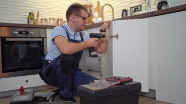 Mutfak dolabının kapısını kablosuz matkapla monte eden üniformalı profesyonel bir tamirci.