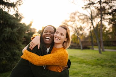 İki neşeli çoklu etnik kadın arkadaş dışarıda kucaklaşıyorlar, gülüyorlar ve birlikte eğleniyorlar.