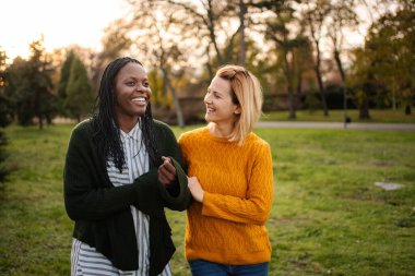 İki farklı kadın birlikte gülüyor, dışarıda eğleniyorlar.