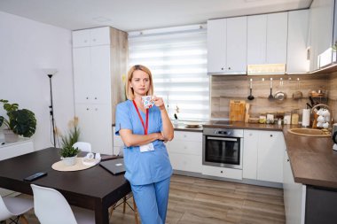 Kadın doktor modern mutfağında mola veriyor, bir fincan kahvenin tadını çıkarıyor.