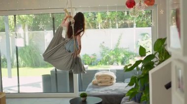 Uzun saçlı çekici genç kız sallanıyor sallanan bir sandalyede oturma odasında ağır çekimde