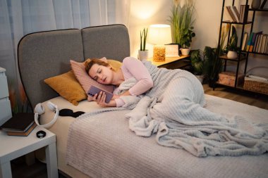 Geceleri cep telefonu kullanan bir kadın yatağında yatıyor.