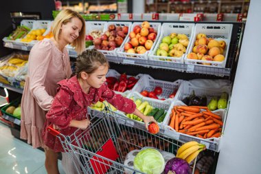 Anne ve kızı taze sebze almak için marketten sebze seçiyorlar.