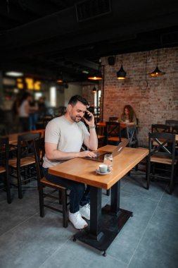 Freelancer bir kafeden uzaktan çalışıyor, telefonla konuşuyor ve bilgisayarında daktilo yazıyor.