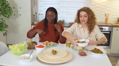 Çok ırklı bayan arkadaşlar ev yapımı taco hazırlarken yemek yiyip sohbet ediyorlar.