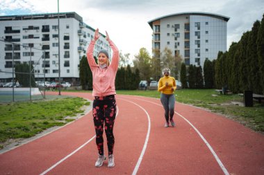 Koşu pistinde egzersiz yapan ve çeşitli spor yapan iki kadın.