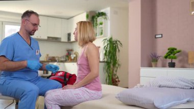 Önlüklü bir tıp çalışanı, ev ziyareti sırasında PCR testi için genç bir kadından örnek alıyor.