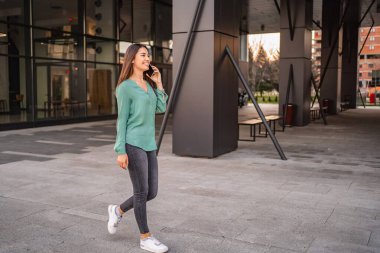 Modern ofis binasının yakınında yürüyen ve konuşan genç bir iş kadını.