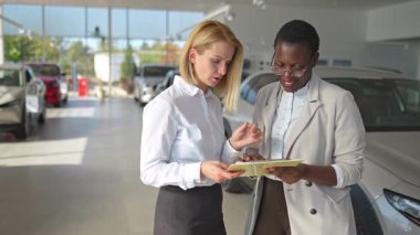 Afro-Amerikalı bir satış temsilcisi araba galerisinde beyaz bir müşteriye danışmanlık yapıyor.