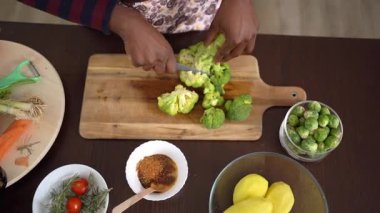 Afrikalı bir kadının mutfakta brokoli keserken yüksek açılı, yavaş çekim görüntüsü.