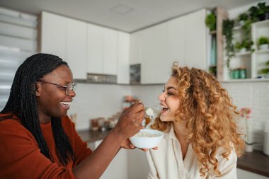 Mutlu kadınlar kahvaltı gevreği yiyor ve modern bir mutfakta birlikte eğleniyorlar.