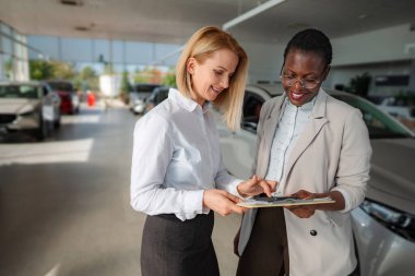 Saleswoman and customer smiling while reviewing documents in a modern car showroom