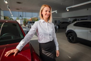 Modern bir araba galerisinde, yeni kırmızı bir arabanın yanında duran satış elemanı.