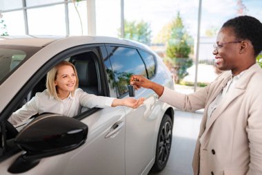 Modern araba galerisindeki satış temsilcisinden araba anahtarı alan mutlu bir müşteri.