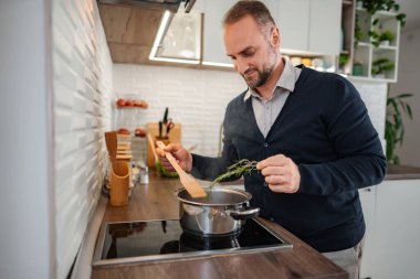 Adam, indüksiyon sobasındaki bir tencere taze biberiye ekliyor.
