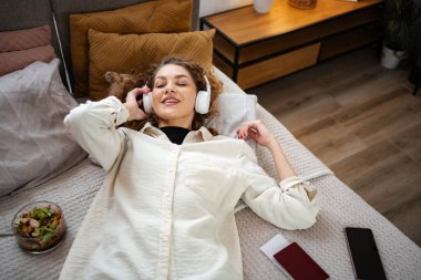 Yatakta müzik dinleyen bir kadın. Pasaportu da yanında. Bir yolculuk bekliyor.