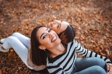 İki kız kıpır kıpır gülen yaprakların arasında otururken kıpır kıpır sonbahar havasında bir neşe anlarını paylaşıyorlar..