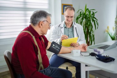 Bir doktor hastaların tansiyonlarını dikkatlice ölçerken not alır..