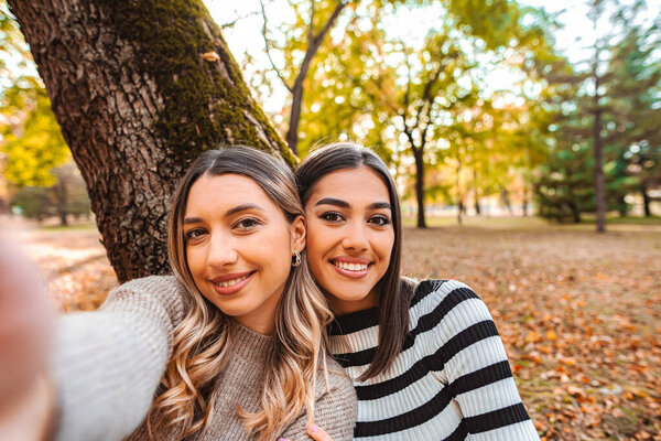 Two girls smile warmly while enjoying a beautiful autumn day in the park surrounded by colorful leaves.