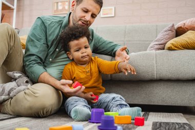 Neşeli bir baba ve oğul evin içinde renkli bloklarla oynarlar..