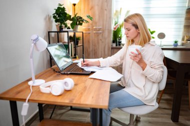 Parlak bir odada dizüstü bilgisayarla çay içen bir kadın..