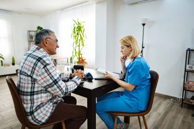 Bir tıp uzmanı yaşlı bir adamla sağlığı tartışıyor..