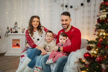 Ebeveynler ve iki çocuk rahat bir koltukta oturup, Noel boyunca evde gülümsüyorlar.